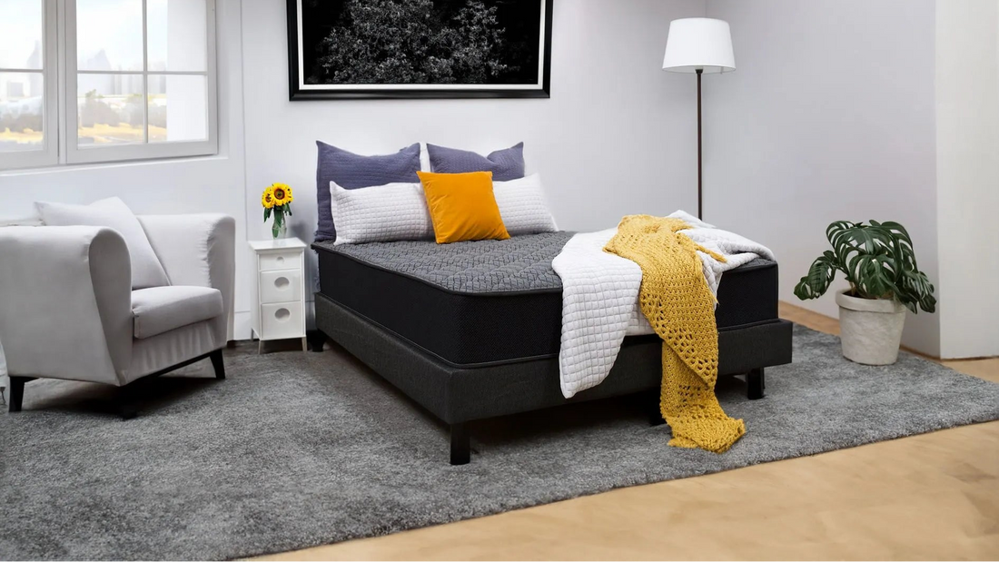 Modern bedroom with dark firm mattress, gray and yellow bedding, white armchair, and floor lamp